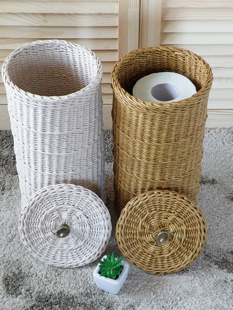Puede incluir: Dos cestas tejidas con tapas, una blanca y otra marr&oacute;n, para guardar rollos de papel higi&eacute;nico. Las cestas est&aacute;n hechas de materiales naturales y tienen un aspecto r&uacute;stico.