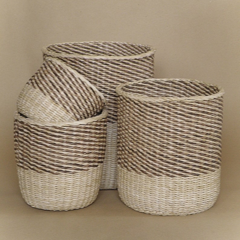 May include: A set of three cylindrical baskets crafted from woven natural fibers. Each basket features a two-tone design with a dark brown upper section and a light beige lower section, showcasing a consistent diagonal rope-like texture throughout.