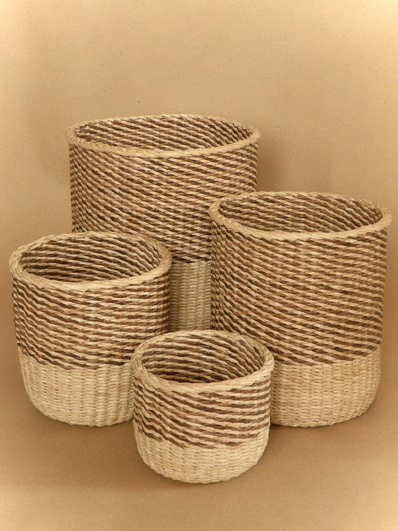 May include: A set of four cylindrical baskets woven from natural fibers. Each basket features a two-tone design with a light beige base and a spiraling pattern of dark brown and light beige twisted rope texture covering the upper portion.