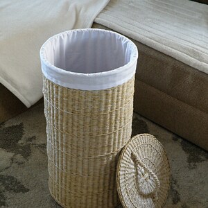 May include: A woven wicker laundry hamper with a white fabric liner and a matching lid. The hamper is empty and sitting on a patterned rug.