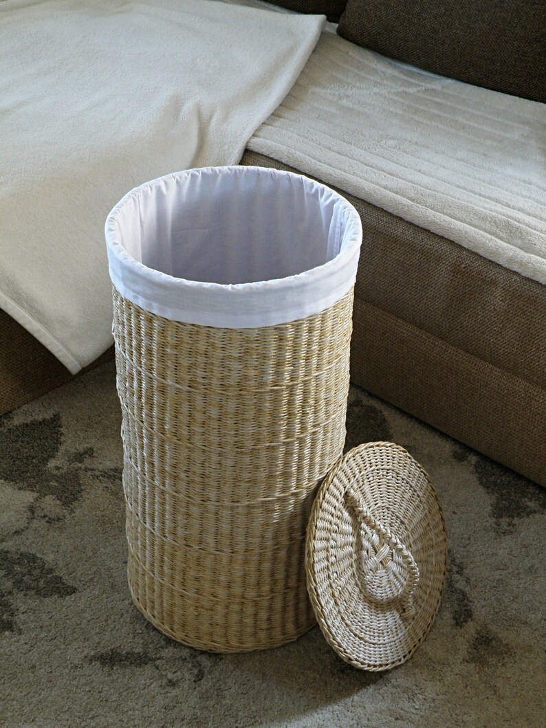 May include: A woven wicker laundry hamper with a white fabric liner and a matching lid. The hamper is empty and sitting on a patterned rug.