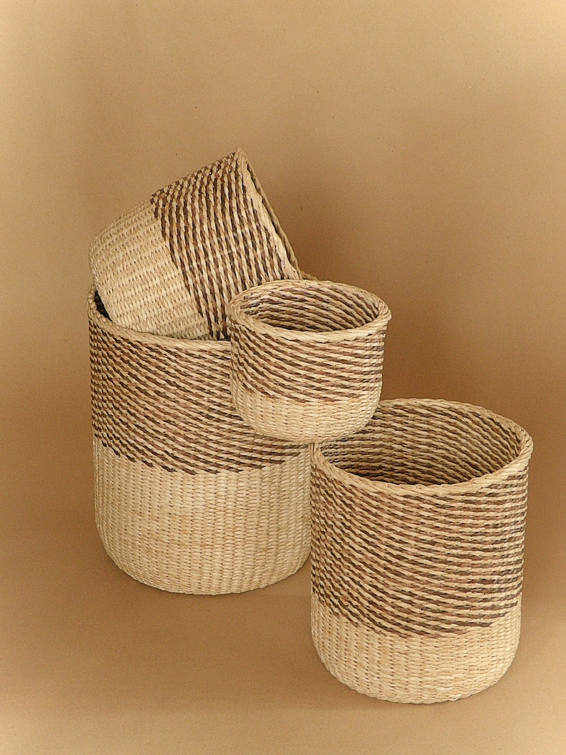 May include: A set of three cylindrical woven baskets featuring a two-tone design. Each basket is constructed with light beige natural fibers at the base and a contrasting dark brown woven pattern around the upper section, creating a distinct visual divide.