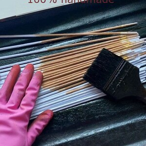 May include: A close-up of a hand wearing a pink glove, smoothing out a stack of white and brown paper strips. The strips are arranged in a tray, and a black paintbrush is lying on top of the stack. The text "100% handmade" is visible at the top of the image.