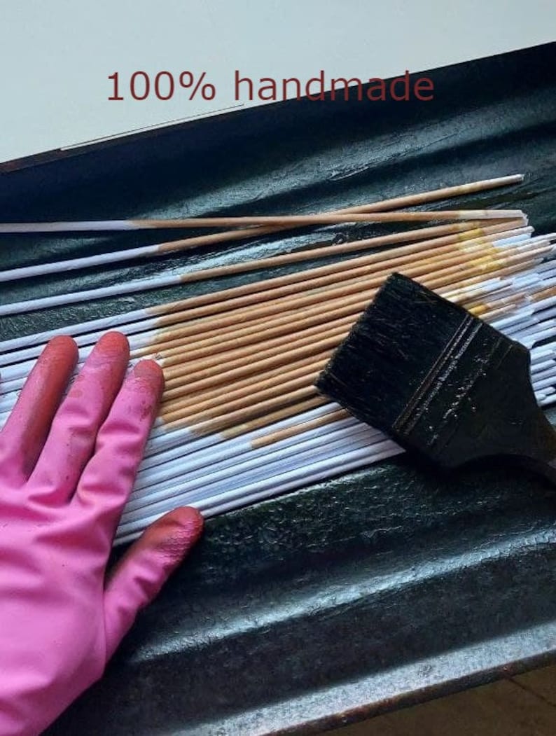 May include: A close-up of a hand wearing a pink glove, smoothing out a stack of white and brown paper strips. The strips are arranged in a tray, and a black paintbrush is lying on top of the stack. The text "100% handmade" is visible at the top of the image.