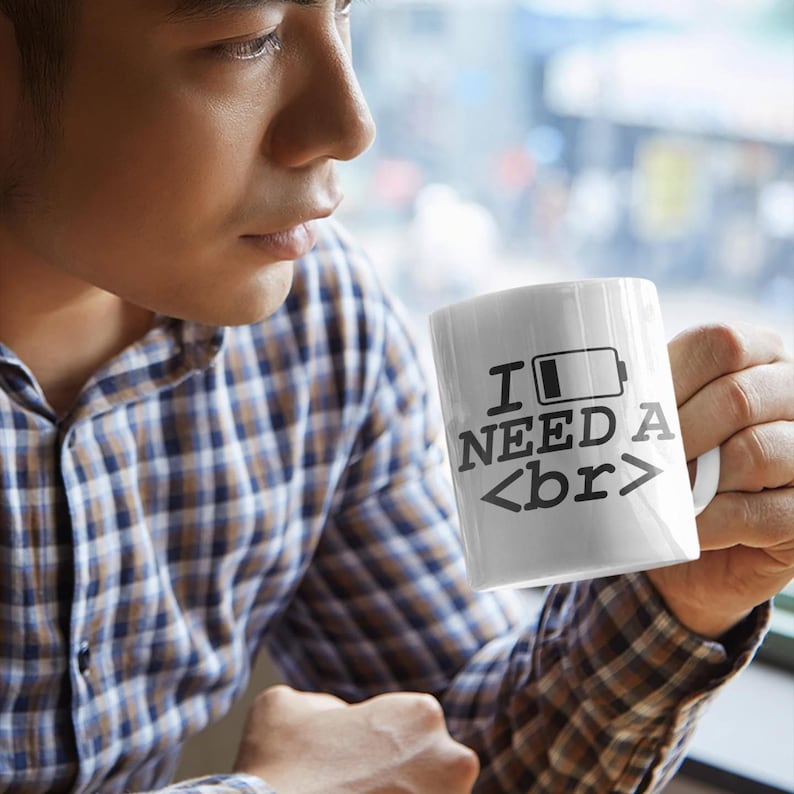 Puede incluir: Taza de caf&eacute; blanca con texto negro que dice "I need a <br>" con un icono de bater&iacute;a vac&iacute;o. La taza est&aacute; siendo sostenida por una persona.