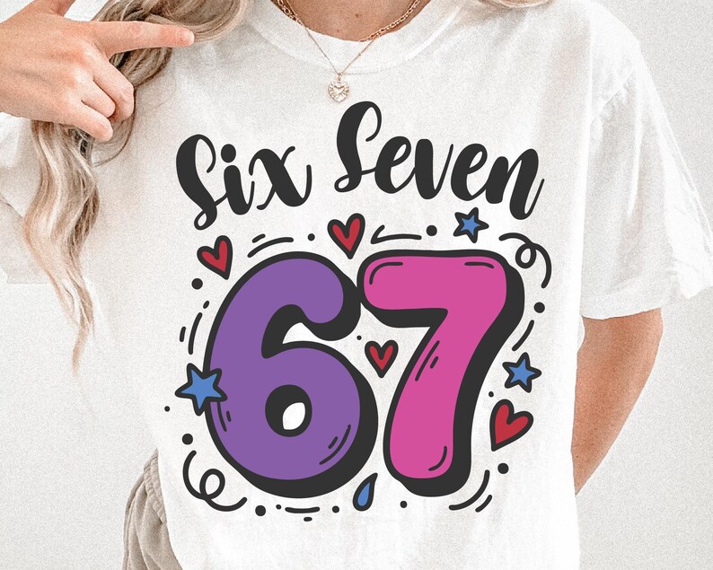 May include: White t-shirt featuring the words "Six Seven" in black script above a large, colourful "67" in purple and pink. The design includes red hearts, blue stars, and decorative swirls.
