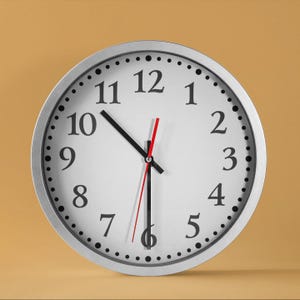 May include: A silver analogue clock with black numbers and hands on a white face. The clock is set to 12:00.