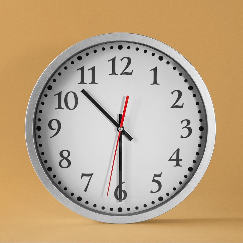 May include: A silver analogue clock with black numbers and hands on a white face. The clock is set to 12:00.