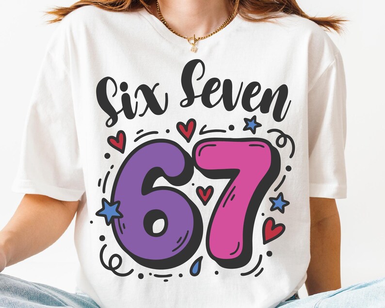 May include: White t-shirt featuring the words "Six Seven" in black script. The numbers "67" are in purple and pink, outlined in black, with hearts and stars. A gold necklace is visible.