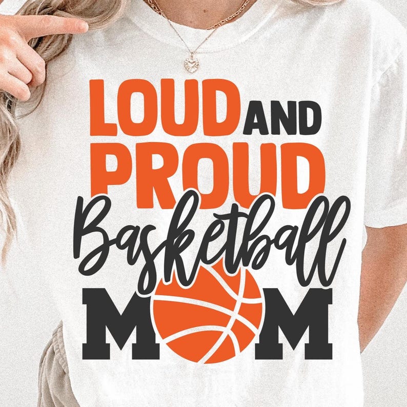 K&ouml;nnte beinhalten: Wei&szlig;es T-Shirt mit dem Text "LOUD AND PROUD Basketball MOM" in Orange und Schwarz. Das Wort "Basketball" ist in einer Schreibschrift geschrieben, und eine Basketball-Grafik befindet sich in der Mitte.