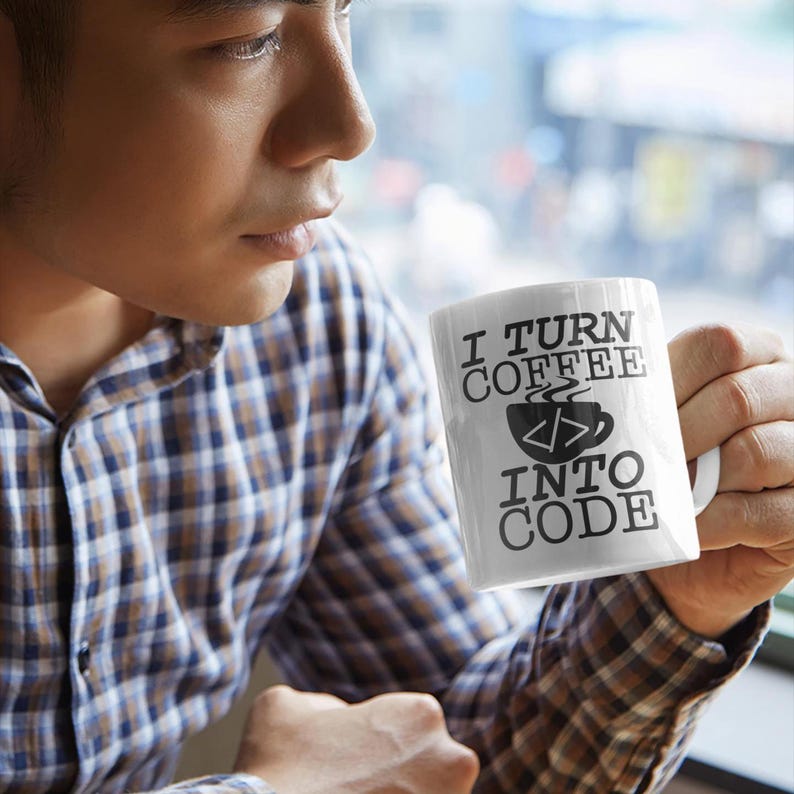 Puede incluir: Taza de caf&eacute; de cer&aacute;mica blanca con texto negro que dice "I turn coffee into code" y una imagen estilizada de una taza de caf&eacute; con s&iacute;mbolos de c&oacute;digo.