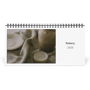 May include: A spiral-bound calendar featuring a photograph of pottery. The image shows a plate, a small bowl, and a textured vase on a draped cloth. The calendar's cover reads "Pottery 2026".