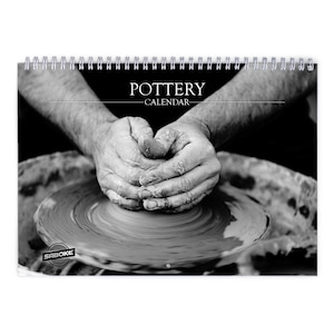 May include: A black and white wall calendar titled POTTERY CALENDAR with a spiral binding at the top. The cover features a high-contrast photograph of hands shaping clay on a pottery wheel, with the brand name SABOKE printed in the bottom left corner.