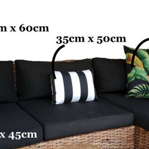 May include: A black wicker sectional sofa with five black and white striped throw pillows, two black and white geometric throw pillows, and two tropical leaf print throw pillows. The pillows are labelled with their dimensions in centimetres.