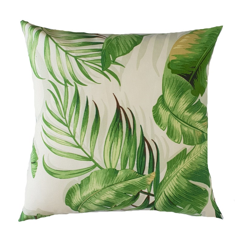 May include: A white cushion with a green tropical leaf pattern. The cushion features a variety of green leaves, including palm leaves and banana leaves.