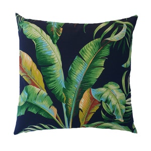 May include: A navy blue cushion with a tropical leaf pattern. The cushion features large green banana leaves with hints of yellow and orange.