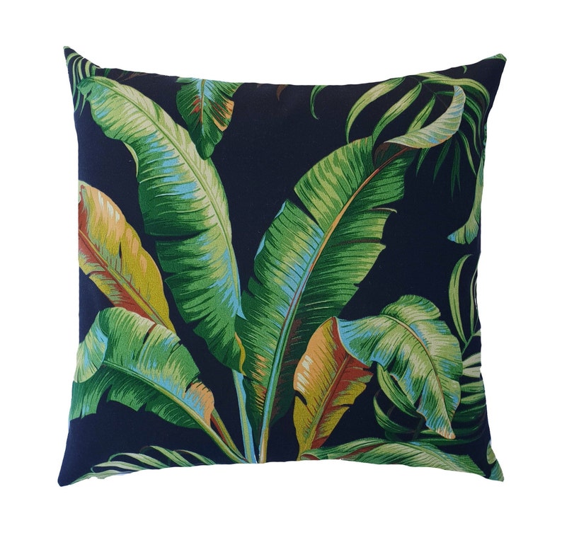 May include: A navy blue cushion with a tropical leaf pattern. The cushion features large green banana leaves with hints of yellow and orange.