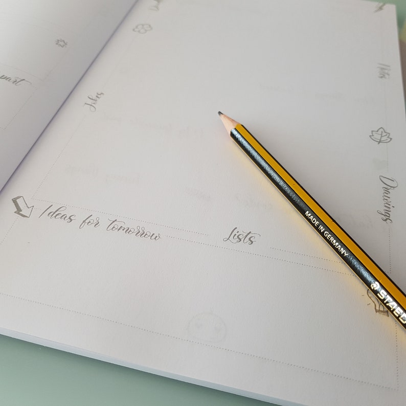 May include: A blank page in a notebook with the words "Ideas for tomorrow" and "Lists" written in cursive. A yellow pencil with a black eraser is lying on the page.