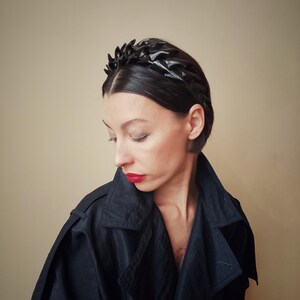 May include: A black headband with a geometric design. The headband is made of a shiny material and has a pointed shape.