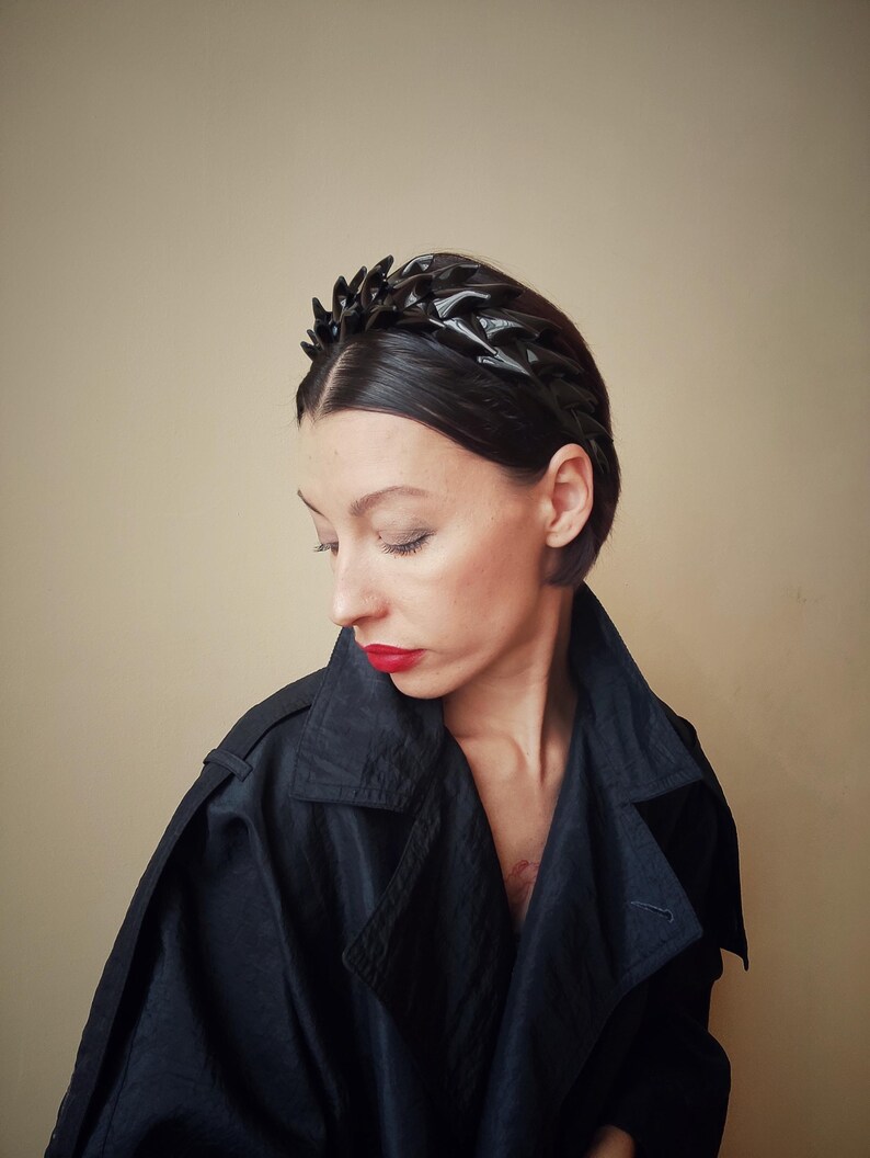 May include: A black headband with a geometric design. The headband is made of a shiny material and has a pointed shape.