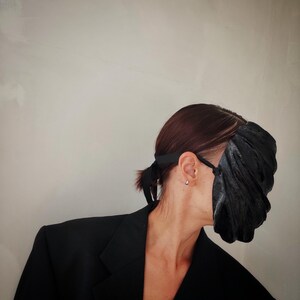 Pu&ograve; includere: Una persona che indossa un blazer nero e una maschera facciale nera con superficie testurizzata.