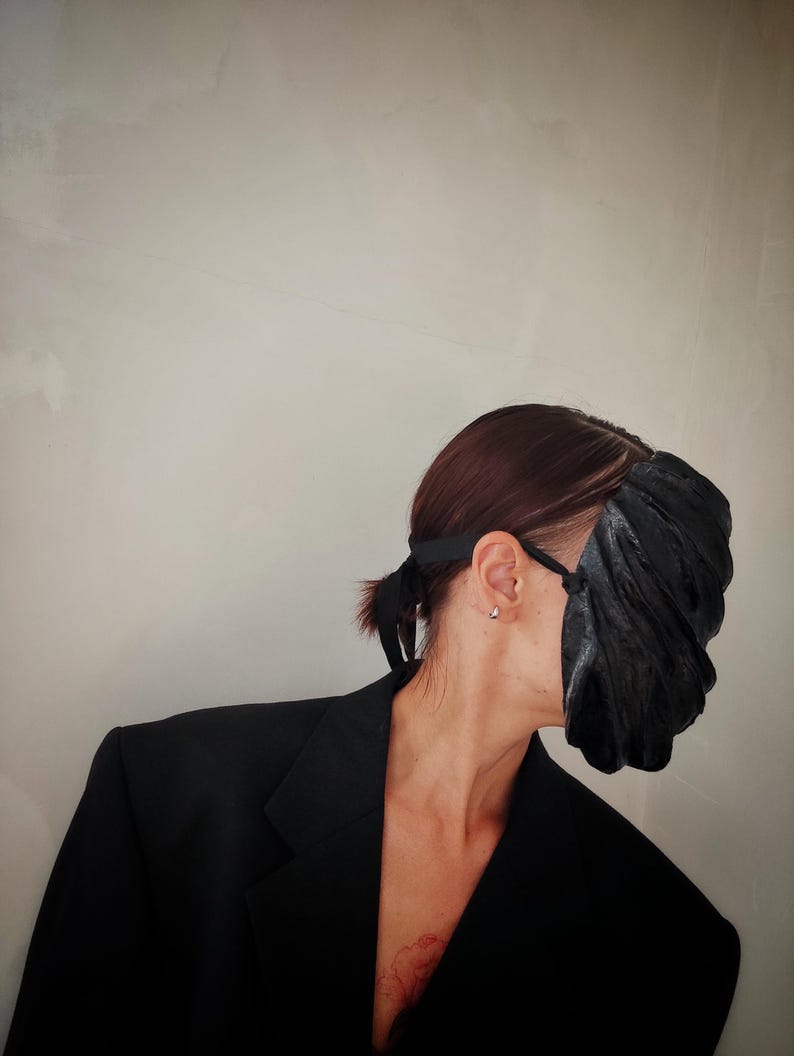 Pu&ograve; includere: Una persona che indossa un blazer nero e una maschera facciale nera con superficie testurizzata.