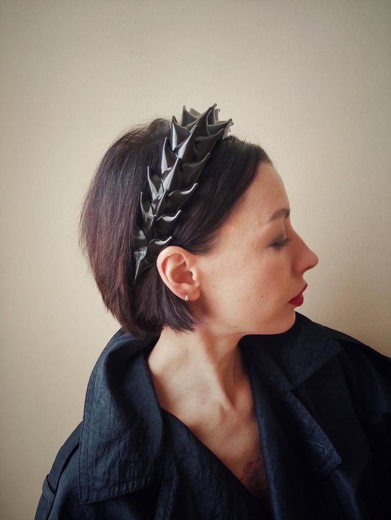 May include: A black headband with a spiky, leaf-like design. The headband is made of a shiny, textured material.