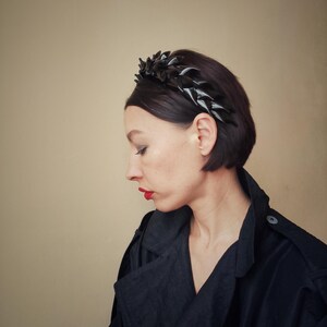 May include: A woman with short dark hair is wearing a black headband with a geometric design. She is wearing a black jacket and has red lipstick on.