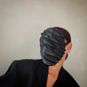 Pu&ograve; includere: Una persona che indossa un blazer nero e una maschera facciale nera con un design testurizzato e stratificato.