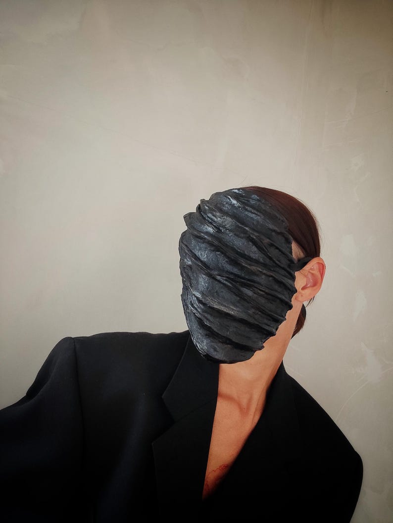 Pu&ograve; includere: Una persona che indossa un blazer nero e una maschera facciale nera con un design testurizzato e stratificato.
