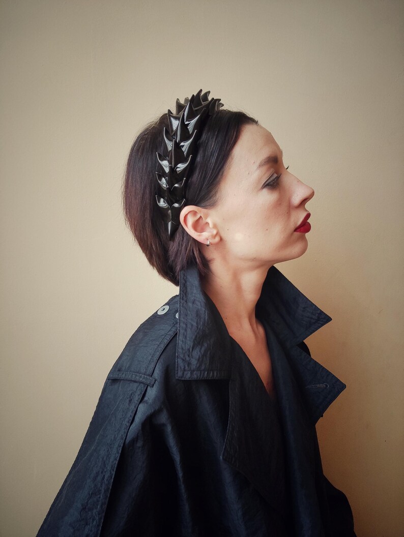 May include: A black headband with a row of sharp, pointed spikes. The headband is worn by a person with short, dark hair.