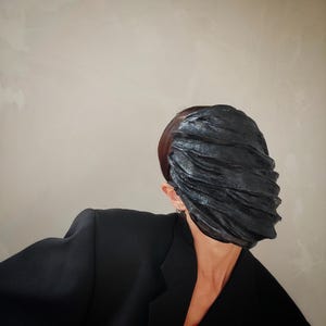 Pu&ograve; includere: Una persona che indossa un blazer nero e una maschera facciale nera testurizzata che copre l'intero viso.