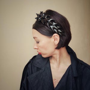 May include: A black headband with a geometric design. The headband is made of a shiny material and has a sharp, angular look.