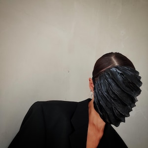 Pu&ograve; includere: Una persona che indossa un blazer nero e una maschera facciale nera con un design plissettato.