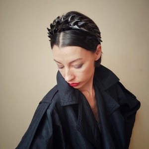 May include: A black headband with a spiky, geometric design. The headband is made of a flexible material and is worn by a person with dark hair.