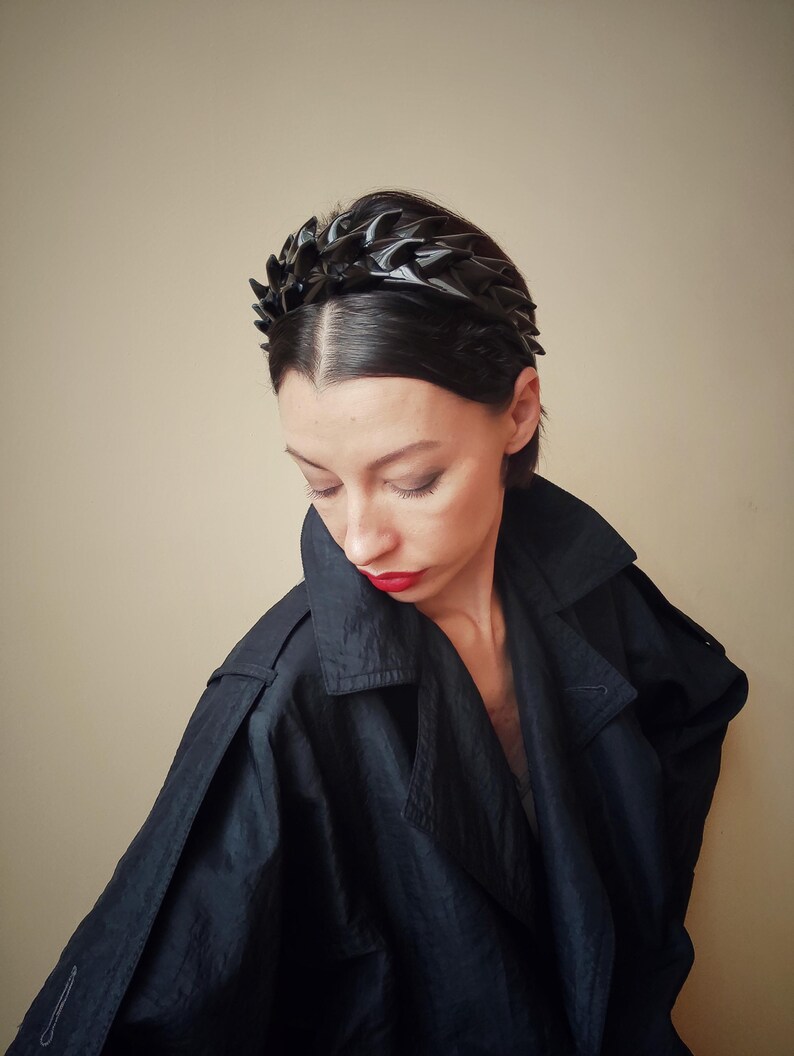 May include: A black headband with a spiky, geometric design. The headband is made of a flexible material and is worn by a person with dark hair.