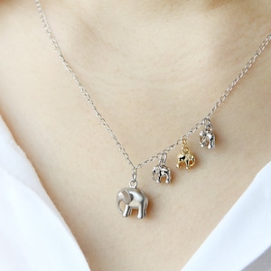 Puede incluir: Un collar de cadena de plata con cuatro pequeños colgantes de elefante. Los colgantes son de plata, oro y una mezcla de plata y oro.
