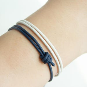 Könnte beinhalten: Zwei Lederarmbänder, eines weiß und eines dunkelblau, mit einem Knoten zusammengebunden.