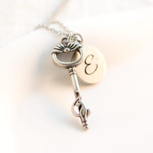 Puede incluir: Un collar de plata con una llave, un pequeño dije de pájaro y un colgante redondo con la letra "E" grabada.