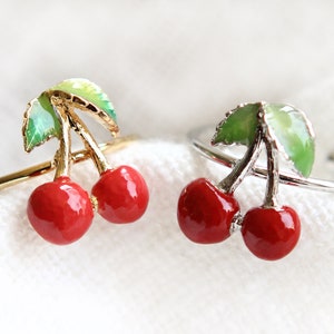 May include: Two adjustable rings with red and green enamel cherry designs, one in gold and one in silver.