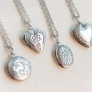 Puede incluir: Tres collares de plata con colgantes de diferentes diseños. Los colgantes son de forma de corazón, ovalados y redondos. Cada colgante tiene un delicado patrón floral.