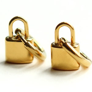 May include: Two gold-colored padlocks with attached rings. The padlocks are closed and have a shiny finish.