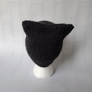 May include: A black knitted cat hat with pointy ears. The hat is on a white mannequin head.