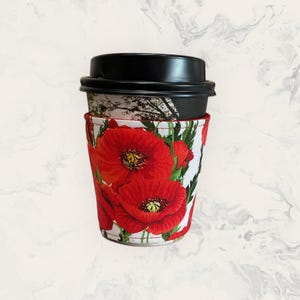 May include: A red poppy floral print coffee cup sleeve. The sleeve is made of fabric and has a white background with red poppies.
