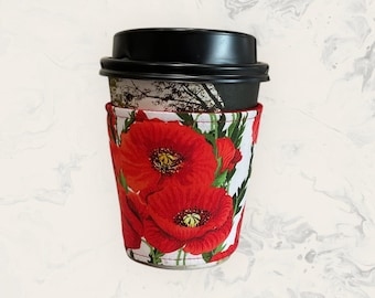May include: A coffee cup sleeve with a red poppy floral print. The sleeve is made of fabric and has a white background with red poppies.