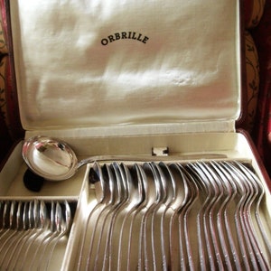 May include: A vintage silverware set in a brown case, featuring numerous silver spoons and a serving spoon. The spoons are neatly arranged in the case, which is lined with cream-colored fabric. The lid of the case displays the word "ORBRILLE".