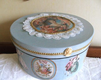 May include: A round, light blue decorative box with a lid. The lid features a portrait surrounded by flowers and a white lace trim. The box is adorned with gold trim and oval cameo accents, and illustrations of people.