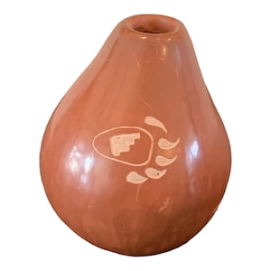 May include: A reddish-brown, pear-shaped ceramic vase with a small opening at the top. The vase features a white bear paw print design on the front. The vase has a smooth, glossy finish.