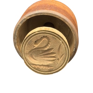 May include: A vintage wooden butter mold with a carved swan design. The mold is made of light-colored wood and has a cylindrical shape. The swan is depicted with its wings spread, and the mold is in excellent condition.