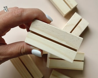 May include: Five natural wood display stands with a slot in the center for holding cards or photos. The stands are arranged in a pile on a light pink surface.